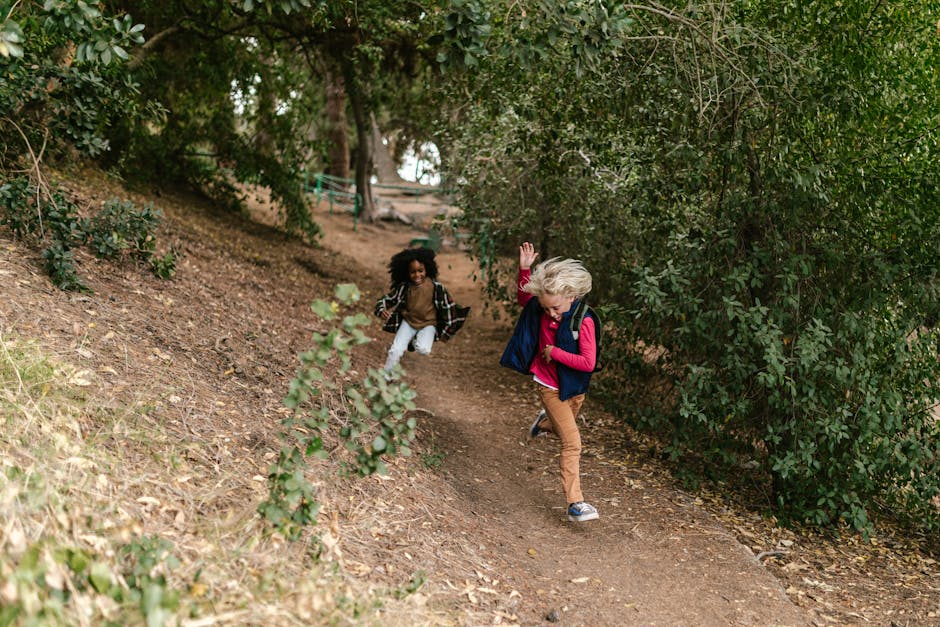 Two children joyfully running along a forest trail, surrounded by lush greenery.