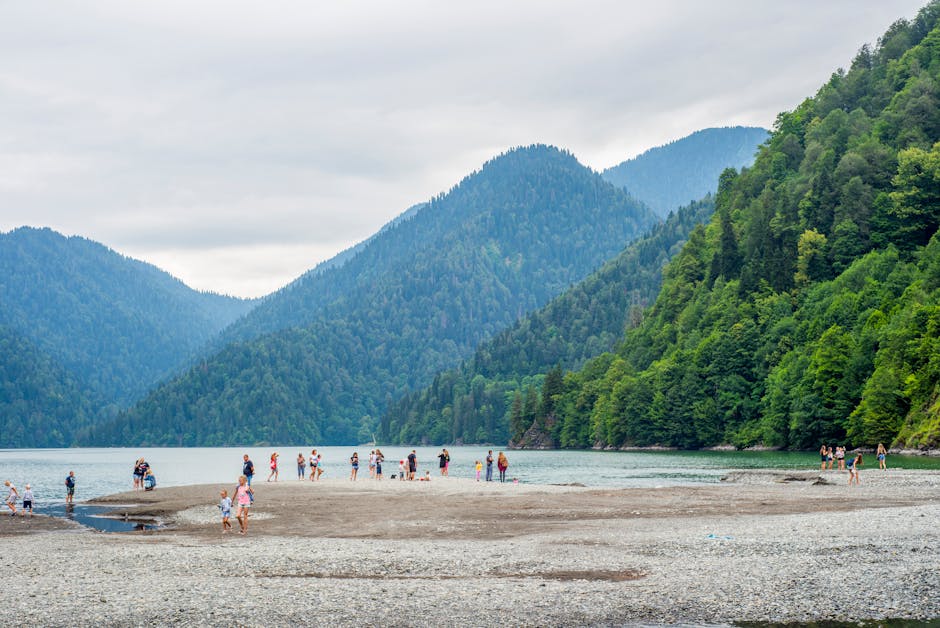 People enjoy a summer day at a lake surrounded by lush green mountains.